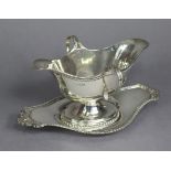 An Edwardian silver double-lipped oval sauce boat & stand with gadrooned rims, the sauce boat with
