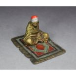 AN AUSTRIAN COLD-PAINTED BRONZE FIGURE OF A CARPET SELLER, seated smoking a pipe, with Bergmann