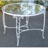 A white painted wrought-iron garden table, inset circular plate glass top, on four pierced scroll