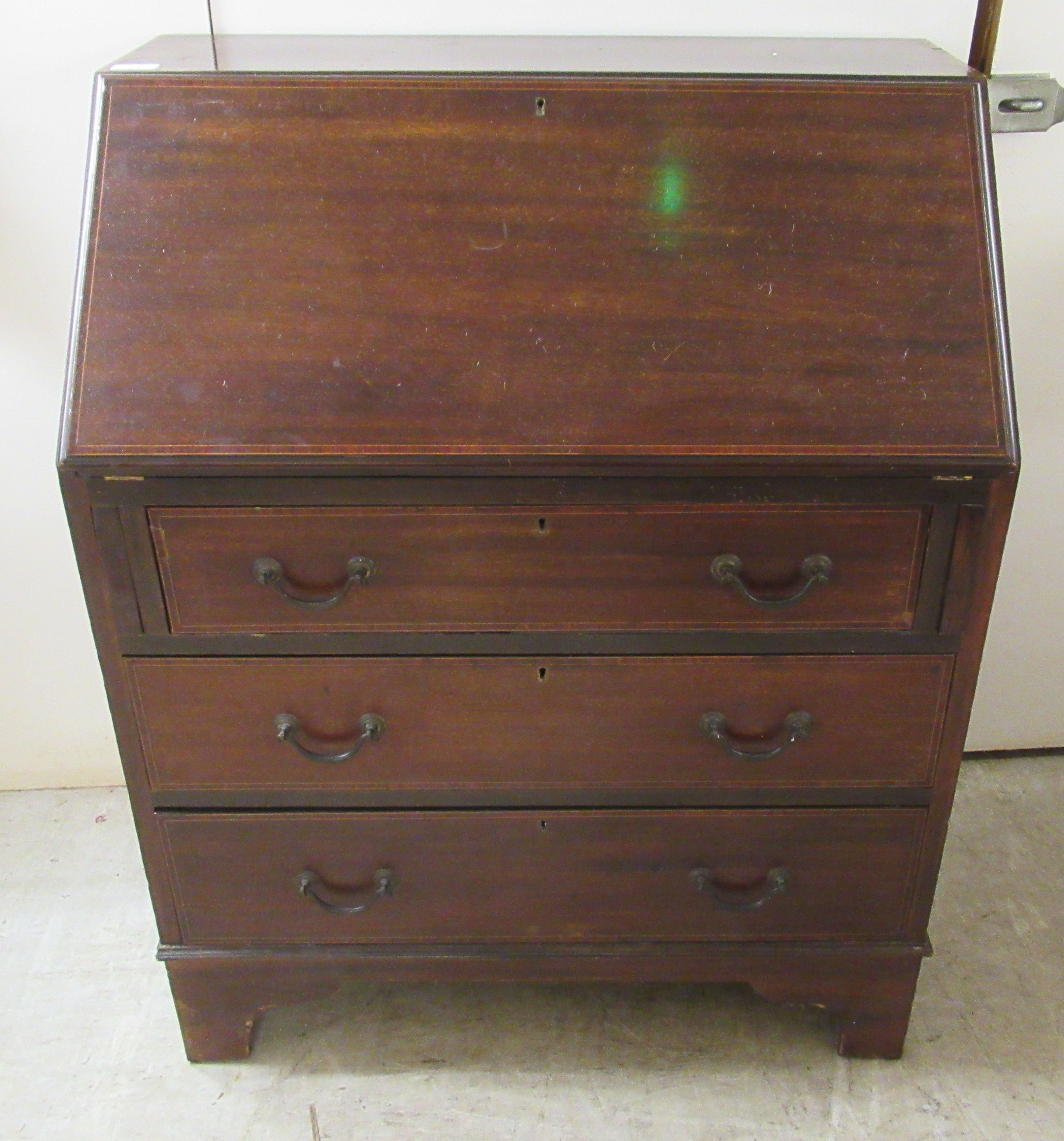 An early 20thC string inlaid mahogany bureau, the fall flap over three long drawers,