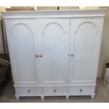 A modern light grey painted pine wardrobe with three arched panelled doors,