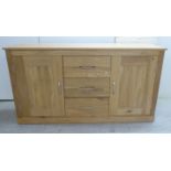 A modern light oak sideboard with a bank of three central drawers,