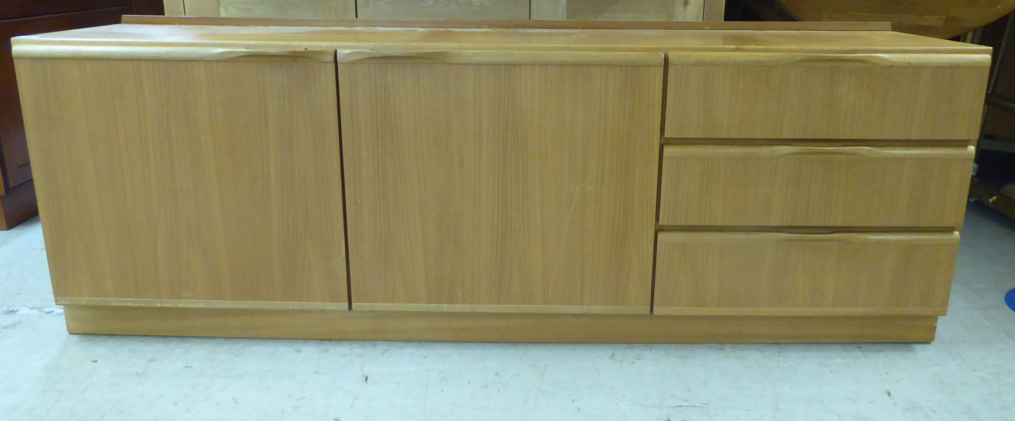 A McIntosh teak sideboard with two doors and a bank of three offset drawers, on a plinth 24''h 70.