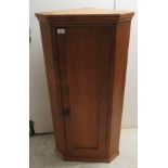 A 20thC honey coloured pine corner cabinet with a panelled door, enclosing three wavy edged shelves,