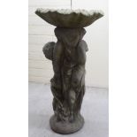 A composition stone bird bath, the wavy edged bowl set over two children,