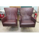 A pair of modern wingback swivel armchair, each upholstered in maroon coloured hide,