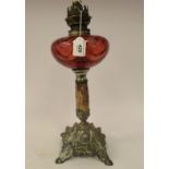 An early 20thC cast metal oil lamp base with a cranberry coloured glass reservoir,