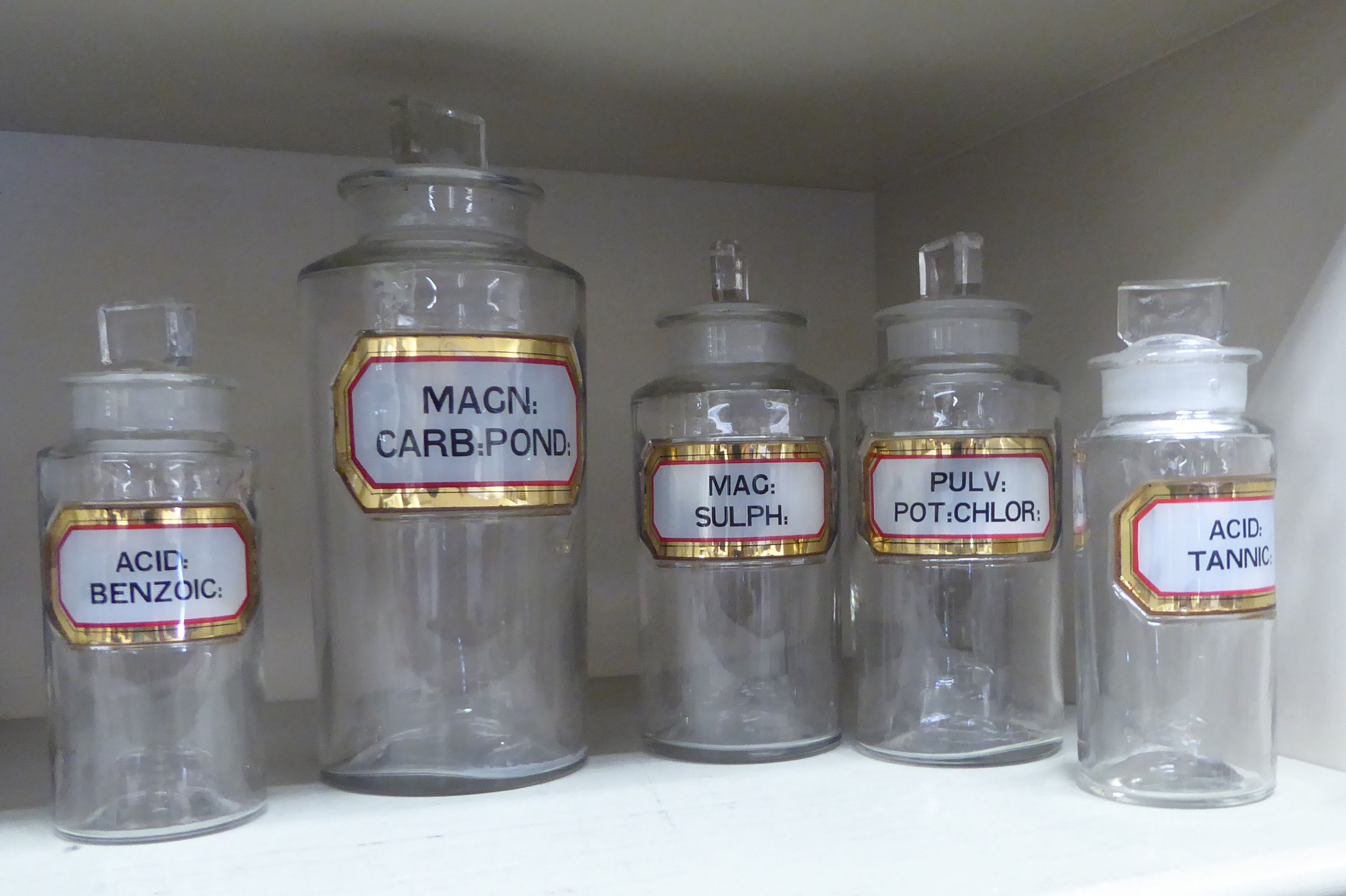 A series of five clear glass chemist's jars of cylindrical form with ground stoppers and labels 6..