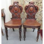 A pair of early Victorian mahogany hall chairs with profusely scroll carved solid backs and waisted
