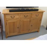 A modern light oak sideboard with three drawers and three cupboard doors, raised on block legs 33"