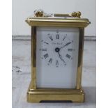 A modern lacquered brass carriage timepiece with bevelled panels and a folding top handle; the