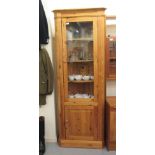 A modern waxed pine corner cupboard, the glazed door enclosing three fixed shelves, over a