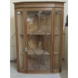 An early/mid 20thC inlaid mahogany hanging corner cabinet, the glazed door enclosing two fixed