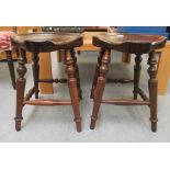 A pair of 20thC mahogany framed saddle stools, raised on splayed, ring turned legs, united by