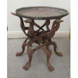 A 20thC African fruitwood occasional table with a copper tray top, raised on folding, interlocking