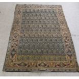 A Persian rug decorated with repeating stylised designs, bordered by floral and foliage, on a