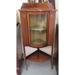 An Edwardian satinwood inlaid mahogany bow front corner cabinet with a glazed door, raised on