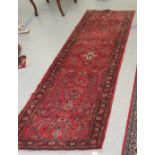 A Persian runner, decorated with floral motifs, on a red ground  106" x 33"