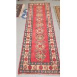 An Afghan Kazak runner, decorated with repeating central diamond shaped motifs, on a multi-