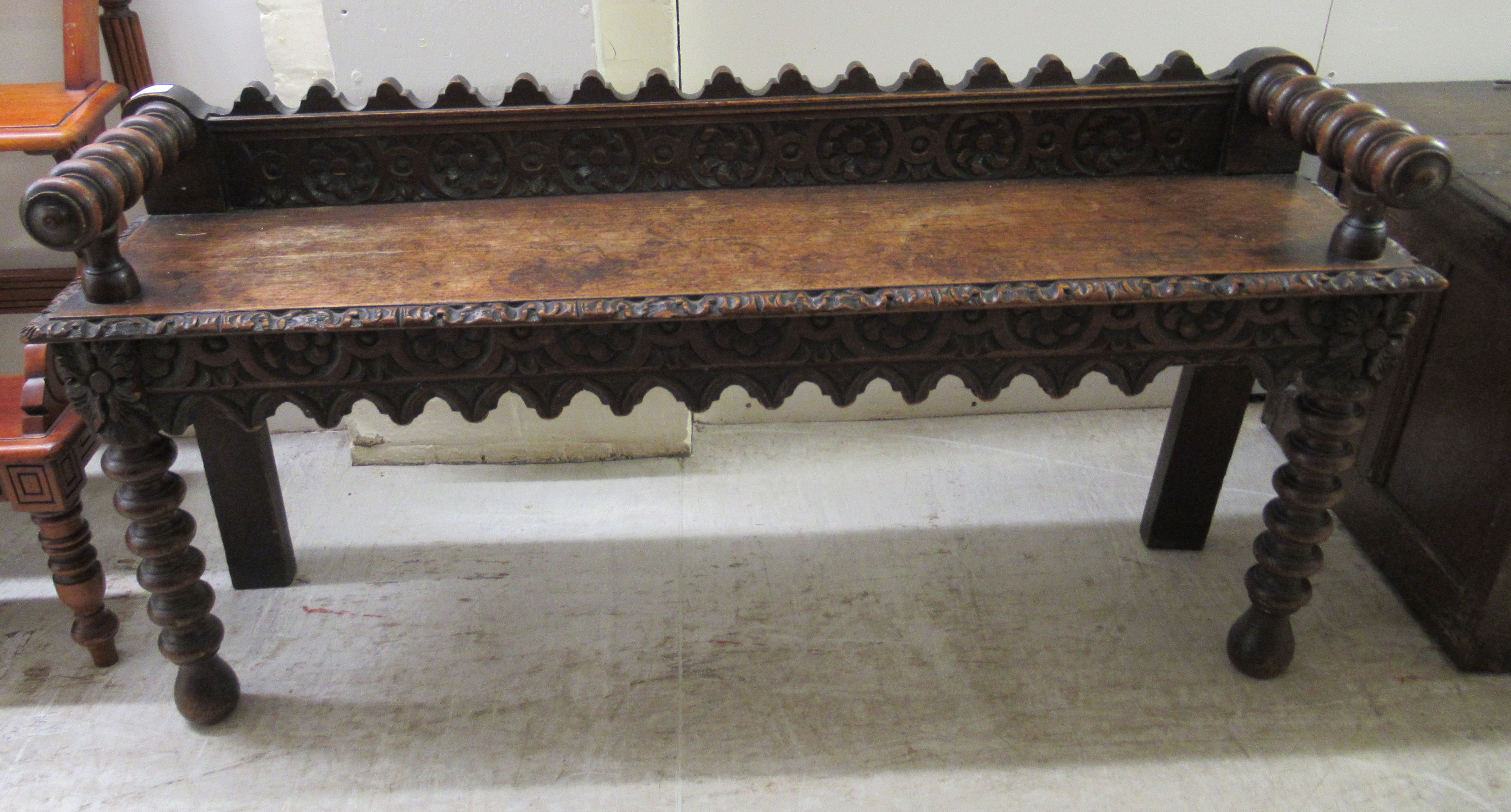 A late Victorian oak window seat with a carved gallery back and turned arms, raised on ring turned