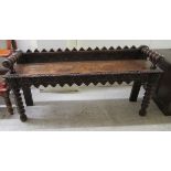 A late Victorian oak window seat with a carved gallery back and turned arms, raised on ring turned