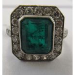 A white gold coloured metal ring, set with a rectangular bevelled cut, emerald coloured central