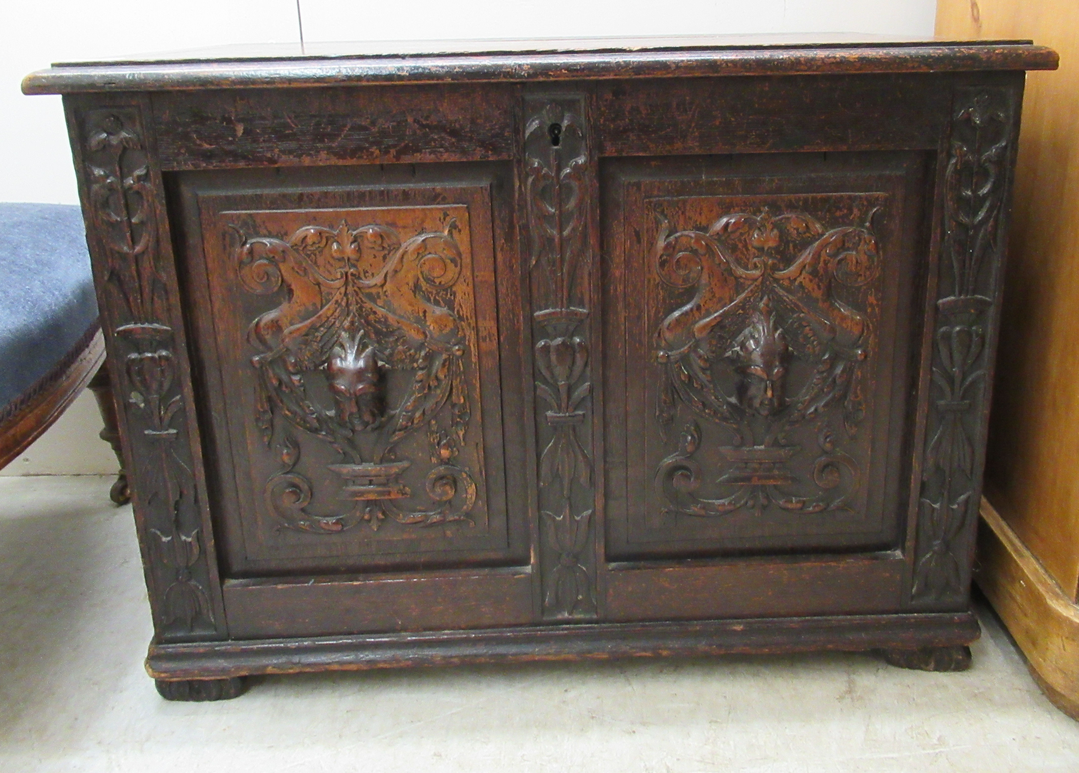 A late Victorian oak coffer with a hinged lid, over a twin panelled front and carved mask motifs, on