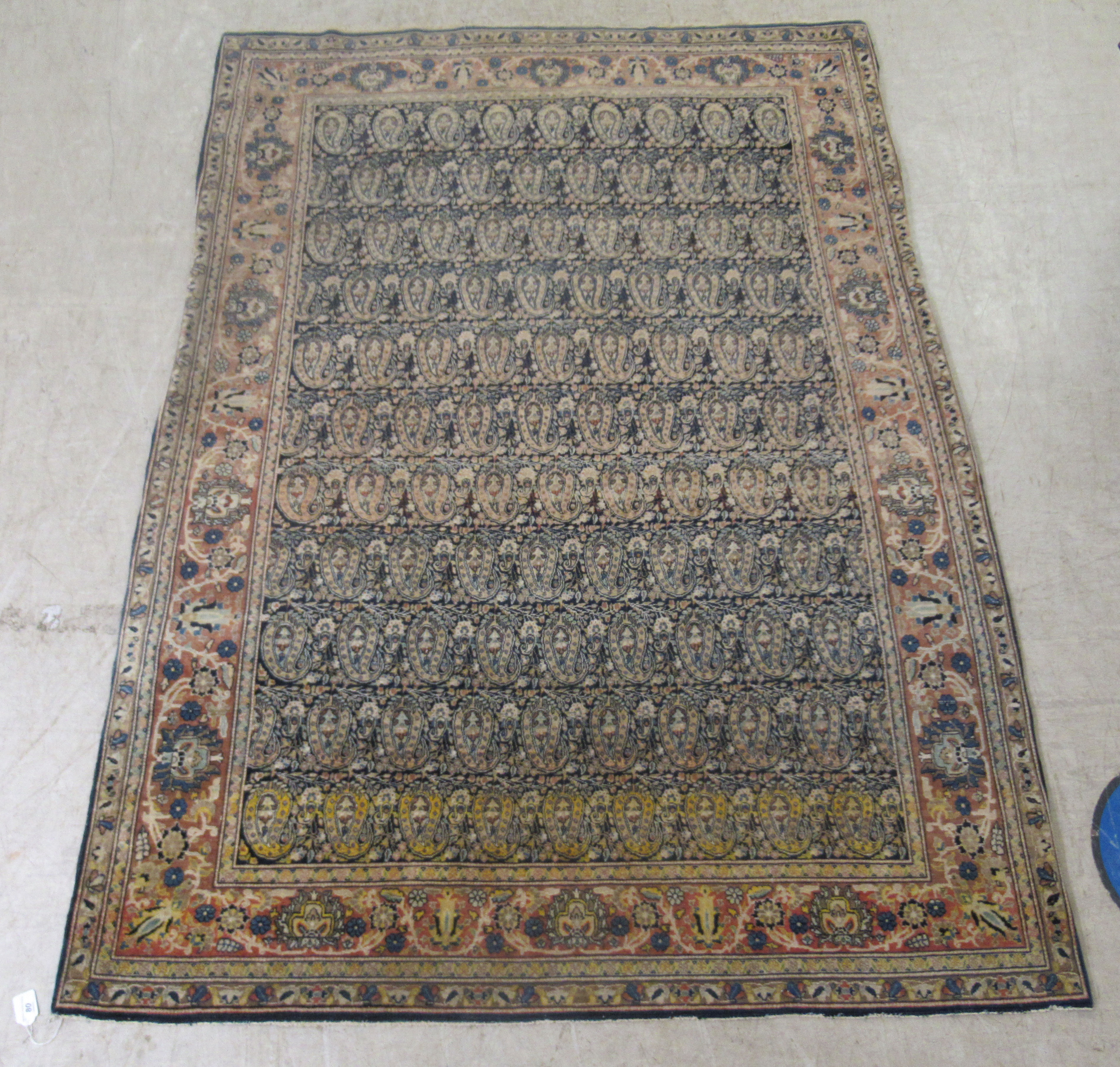 A Persian rug, decorated with repeating stylised designs, bordered by flora and foliage, on a