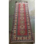 An Afghan Kazak runner, decorated with repeating central diamond shaped motifs, on a multi-