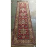 An Afghan Kazak runner, decorated with repeating central stylised decoration, on a red and multi-