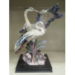 A painted composition sculpture of two exotic birds, standing amongst rocks and flora, on a