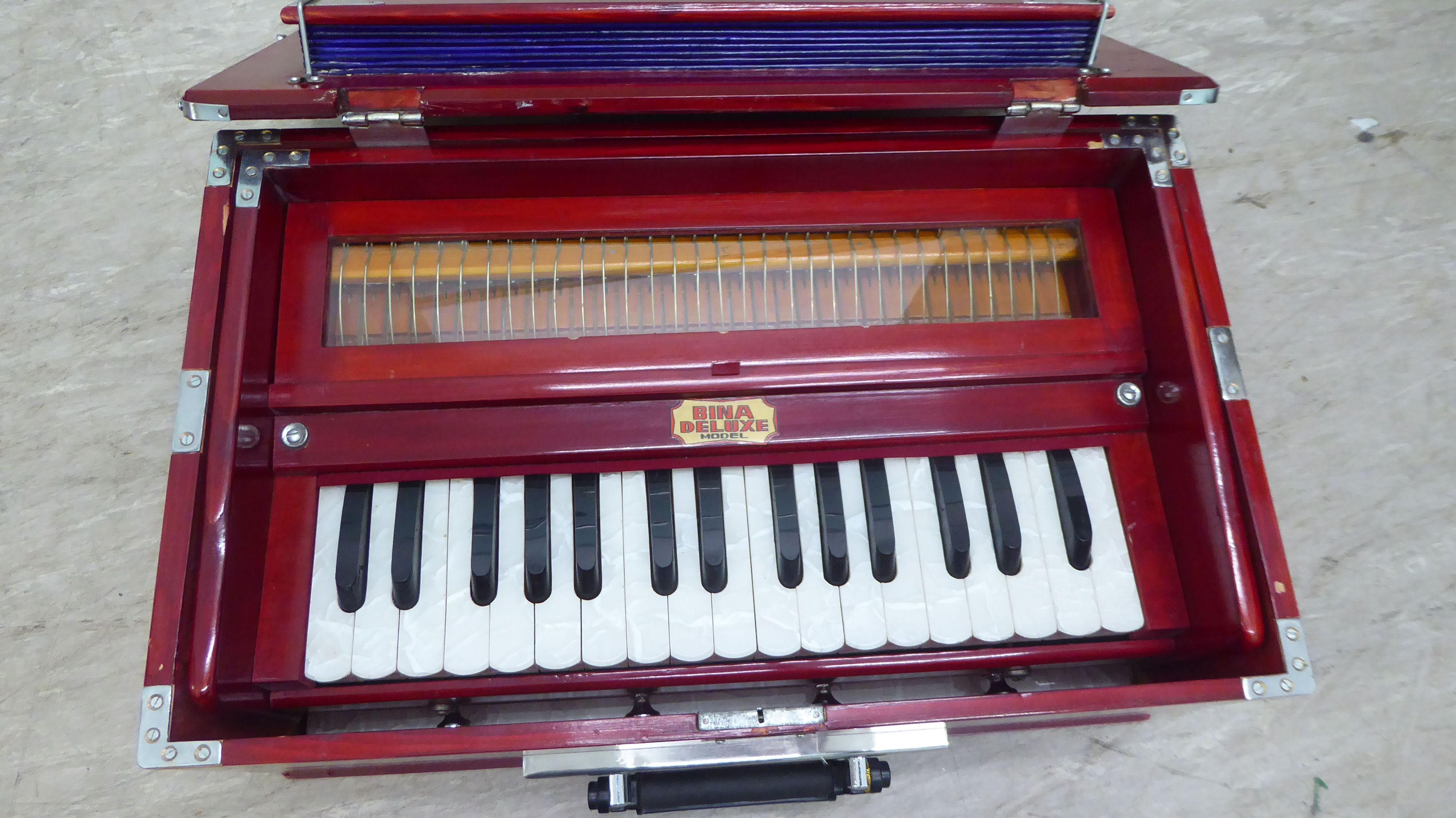 A modern Bina deluxe harmonium, model no.23, retracting into a red stained pine portable table