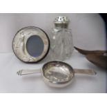 Four silver/white metal items, viz. a twin handled tea strainer; a cut crystal caster with a