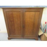 A 1920s stained oak cupboard with a pair of panelled doors, raised on bracket feet  42"h  42"w