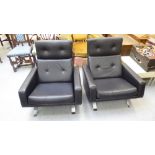 A pair of modern reclined armchairs with angled backs, upholstered in cushioned black vinyl,