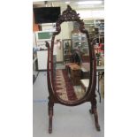 A late Victorian/Edwardian mahogany framed cheval mirror, the oval plate within an ornately carved