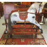 An early 20thC painted dappled grey nursery rocking horse with a studded hide saddle, tail and mane,