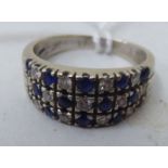 A white coloured gold ring set with three rows of alternating sapphires and diamonds