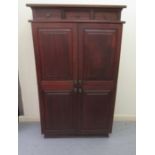 A modern stained teak cabinet with three frieze drawers, over two pairs of panelled doors, on a