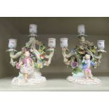 A pair of floral encrusted triple socket candelabra, each featuring a standby cherub figures and