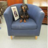 A modern tub style chair, upholstered in navy blue fabric with a cushion seat, raised on turned