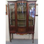 An Edwardian satinwood inlaid mahogany bow front display cabinet with a central drawer, flanked by