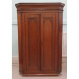 An early 20thC oak and mahogany corner cabinet with a pair of Gothic inspired, arched panelled