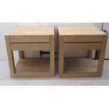 A pair of modern light oak, single drawer lamp tables, raised on block legs, united by a platform