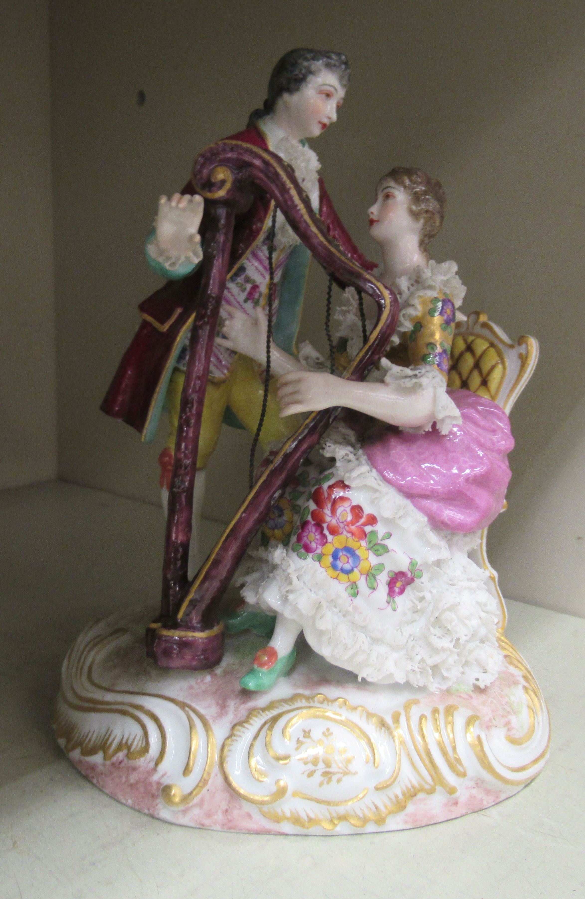 An early 20thC German porcelain group, a seated harpist with her suitor standing alongside, on a