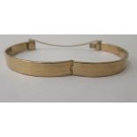 A 9ct gold hinged bangle, on a safety chain