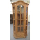 A modern pine corner cabinet with an arched, glazed panelled door, raised on a breakfront plinth and