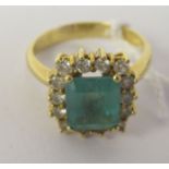 A gold coloured metal (probably 18ct) cluster ring, claw set with an emerald, surrounded by diamonds