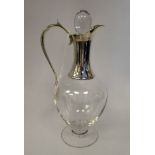 A clear glass and silver mounted pedestal wine jug of bulbous form with a high loop handle,