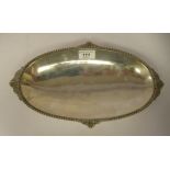 A modern silver coloured metal oval dish with a cast bead border and tab handles, elevated on